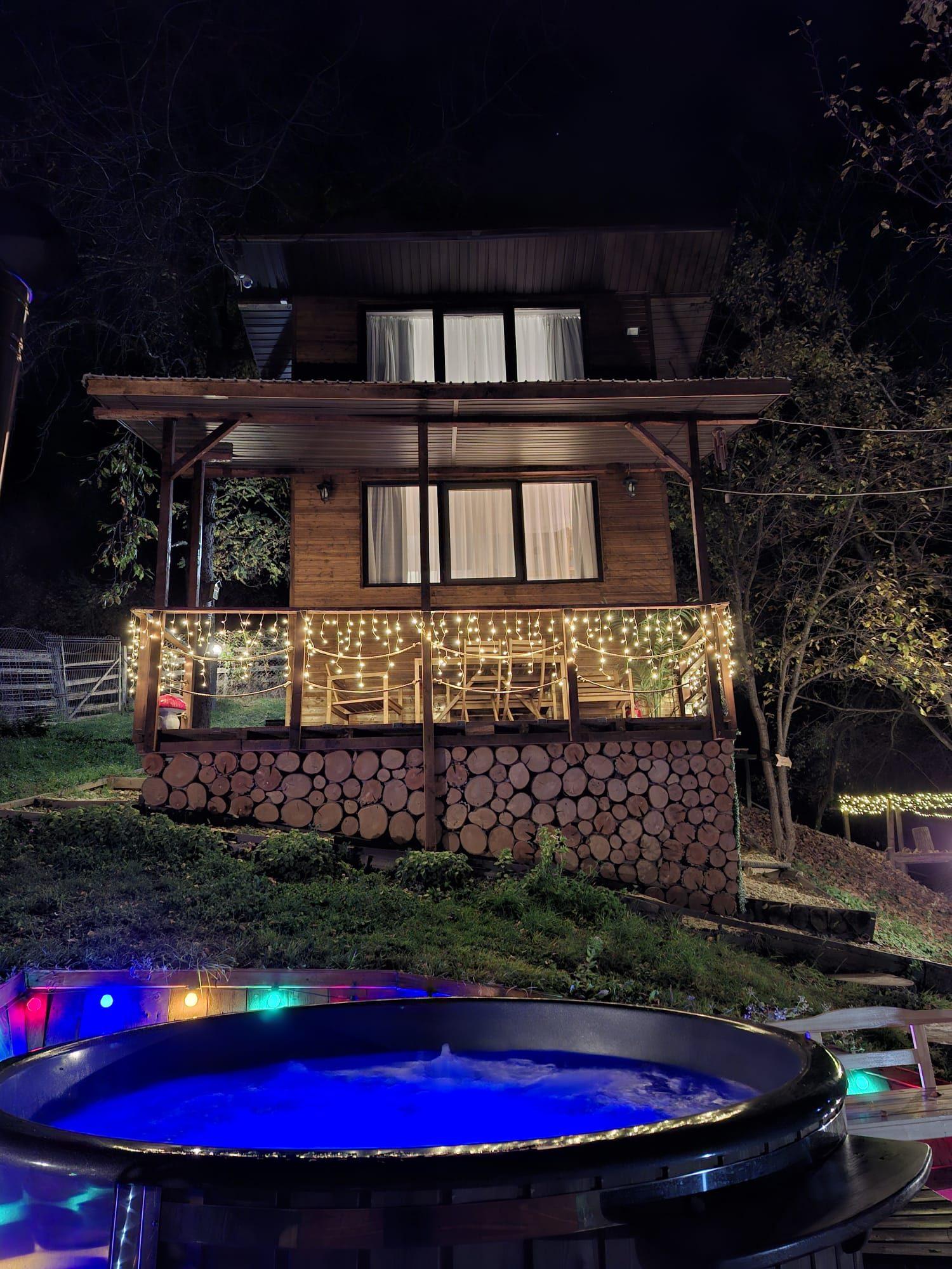 Cabana noaptea cu lumini calde și ciubărul cu apă albastră aprinsă